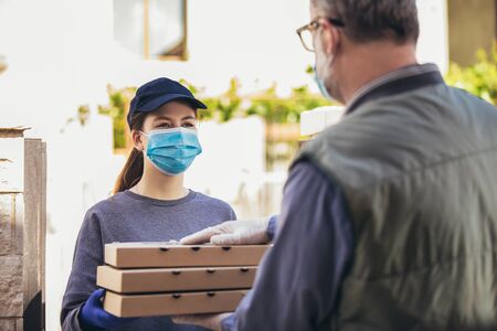 Pizza delivery girl carrying pizza boxes wearing protective mask to an elderly person.の写真素材