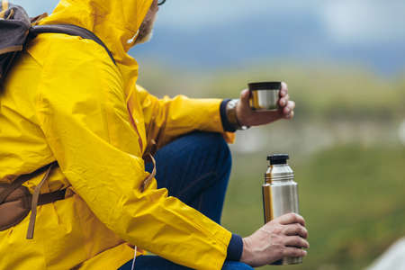 Middle age man with backpack taking break of hiking in a beautiful nature and taking tea or water from a  flaskの写真素材