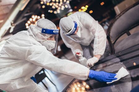 Professional workers in hazmat suits disinfecting indoor of cafe or restaurant, pandemic health risk, coronavirusの写真素材