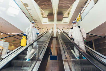 Professional workers in hazmat suits disinfecting indoor of mall, pandemic health risk, coronavirusの写真素材