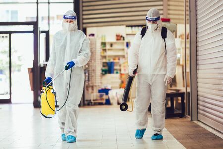 Professional workers in hazmat suits disinfecting indoor of mall, pandemic health risk, coronavirusの写真素材