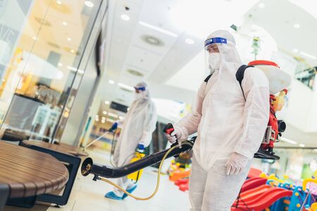 Professional workers in hazmat suits disinfecting indoor of mall, pandemic health risk, coronavirusの写真素材