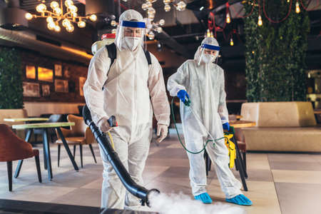 Professional workers in hazmat suits disinfecting indoor of cafe or restaurant, pandemic health risk, coronavirusの写真素材