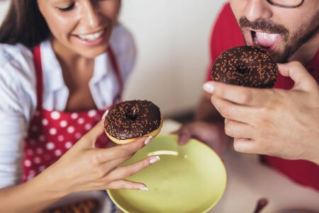 Cheerful young couple having breakfast in kitchen eating donuts.