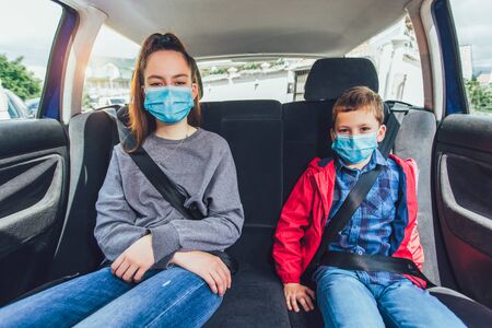 Kids wearing anti virus masks and using digital tablets in the car. Kids are travelling in car during coronavirus outbreakの写真素材