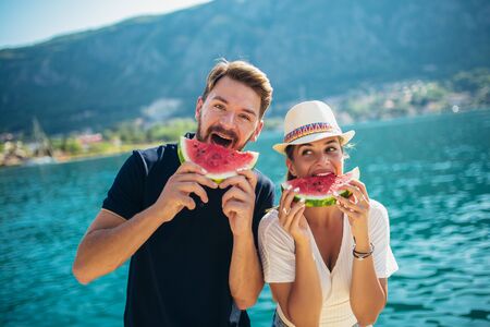 Young smiling couple eating watermelon on the beach having funの写真素材
