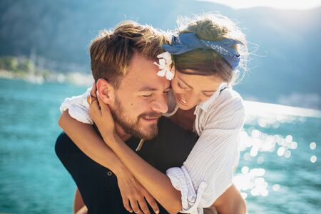 Happy man carrying a woman on his back walking on beach with sea in the background.の写真素材