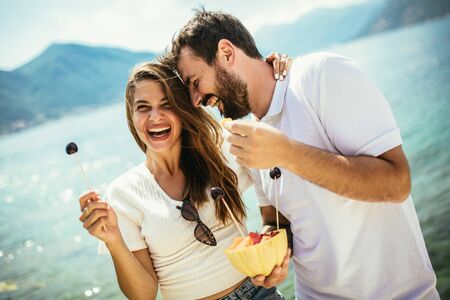 Young happy couple having fun with fruit on the beachの写真素材