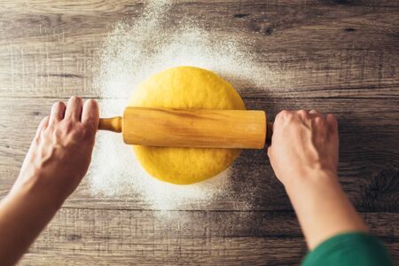 Homemade cooking, female hands roll out pasta with rolling-pin on wooden table.の写真素材