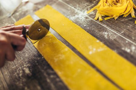 Woman cutting dough for ravioli on table