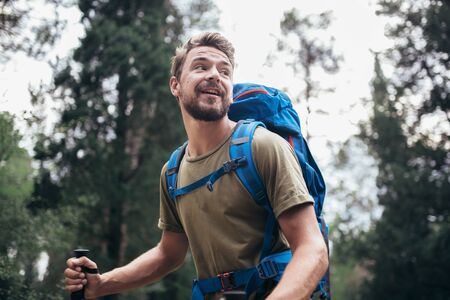 Hiker man with backpack walking in forest in summer. 