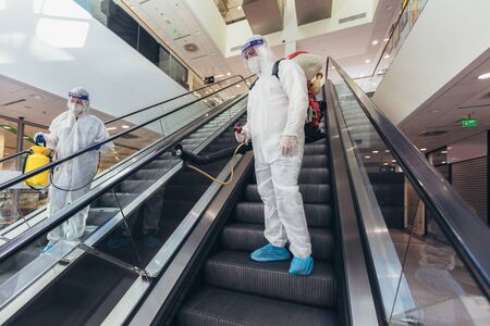 Professional workers in hazmat suits disinfecting indoor of mall, pandemic health risk, coronavirusの写真素材