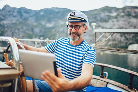 Mature man standing on the deck of his boat and using digital tablet on a sunny afternoon.の写真素材