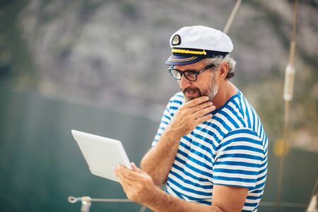 Mature man standing on the deck of his boat and using digital tablet on a sunny afternoon.