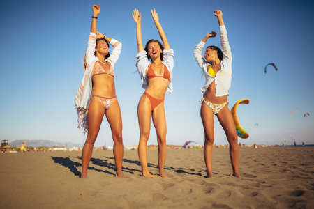 Three friends walking on the beach and laughing on a summer day, enjoying vacation.の写真素材
