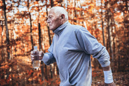 Senior runner in nature. Elderly sporty man running in forest during morning workout. Healthy and active lifestyle at any age conceptの写真素材