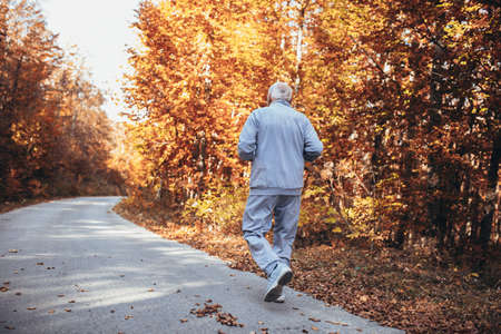 Senior runner in nature. Elderly sporty man running in forest during morning workout. Healthy and active lifestyle at any age conceptの写真素材