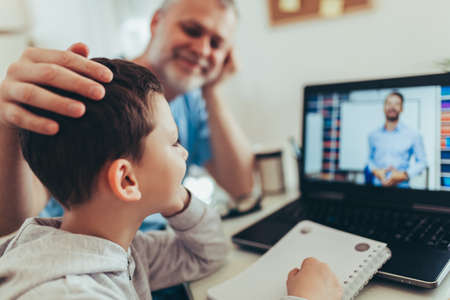 Schoolboy educate online. Father helps his son with home work. Boy in video conference with teacher...