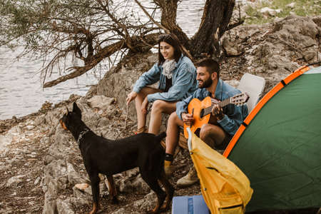 Man and woman and their doberman sitting in chairs outside the tent having coffee and talking....