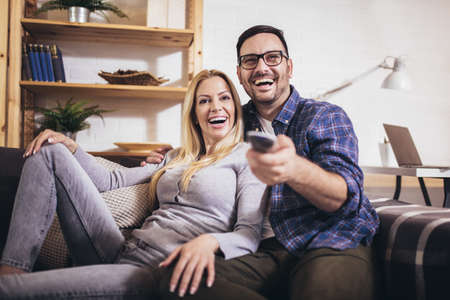 Cheerful couple is watching tv together and having fun in the living room.