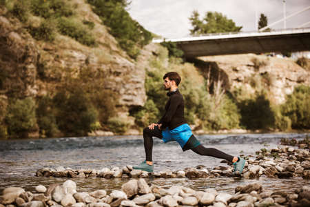 Young male athlete stretching next to the river after morning work out.
