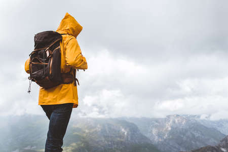 Middle age man traveler in raincoat and backpack enjoying view of mountains.