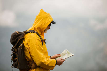 Middle age man traveler in raincoat and backpack using map on hikingの写真素材