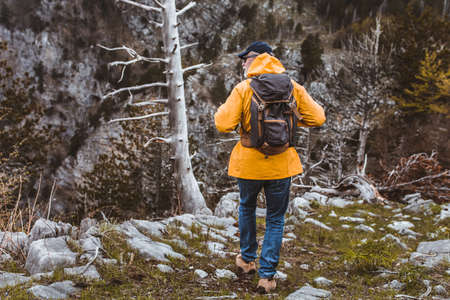 Middle age man traveler in raincoat and backpack enjoying view of mountains.