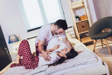 Young smiling cute couple fighting with pillows in the bedroom.の写真素材