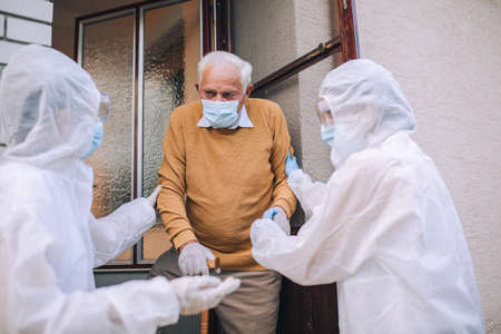 People with protective suits helping senior man outdoors, coronavirus concept.の写真素材