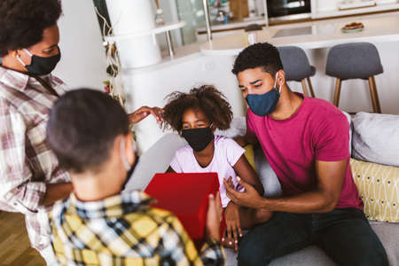African American parents and cute small kids wearing protective masks spending time together at home. Stop the virus and epidemic diseases.の写真素材