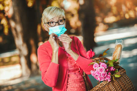 Elderly woman with protective mask holding basket for market.の写真素材