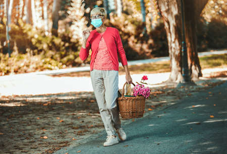 Elderly woman with protective mask holding basket for market.の写真素材