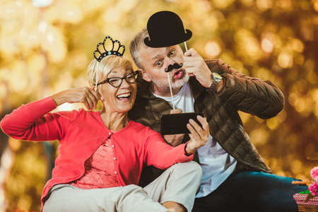 Happy senior couple having a picnic in autumn park make selfie photo.