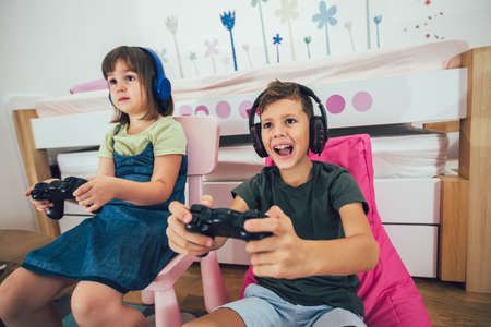 Pretty little girl and boy are playing game console and laughing at home