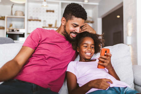 African american father and daughter with smartphone at homeの写真素材