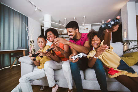 African American family at home sitting in sofa couch and playing video games togetherの写真素材