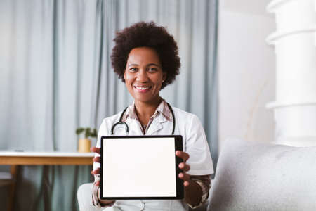 Portrait of happy black healthcare worker holding digital tablet and looking at camera.の写真素材