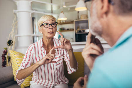 Senior woman talking using sign language with her husband at home.の写真素材
