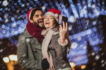 Young beautiful couple with Santa hats make selfie photo outdoor.
