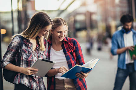 Happy young university students friends studying with books and digital tablet at universityの写真素材