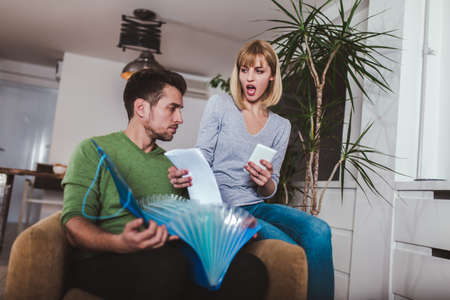 Couple doing accounting on line with a phone bank app sitting on a couch in the living room at home