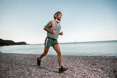 Running man jogging on beach. Male runner training outside working out.
