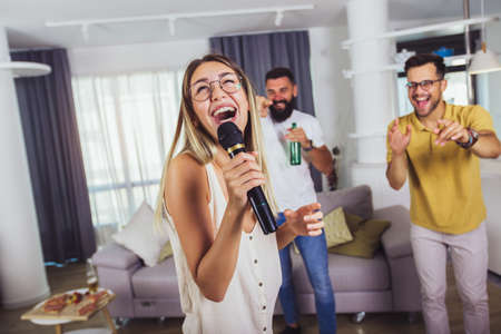 Group of  friends having fun at home. They are drinking beer and having karaoke.
