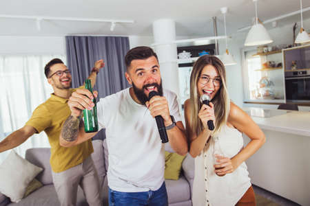 Group of  friends having fun at home. They are drinking beer and having karaoke.の写真素材