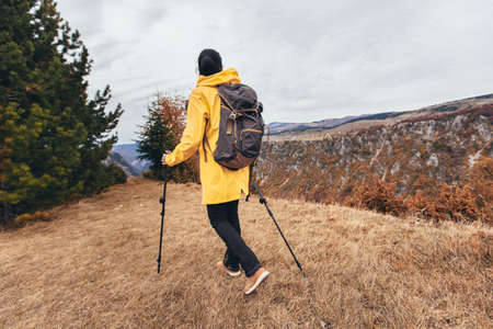 Happy mid age woman with backpack and raincoat standing on top of the mountain