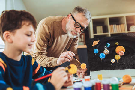 Happy school boy and his father making a solar system for a school science project at homeの写真素材