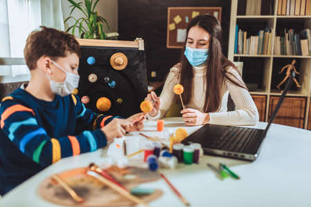 Happy school boy and girl with protective mask making a solar system for a school science project at homeの写真素材
