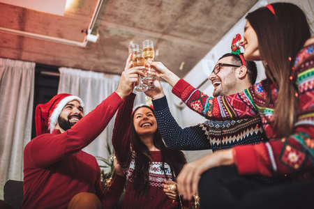 Group of friends sitting in nicely decorated house, having fun while celebrating Christmas or New Yearの写真素材