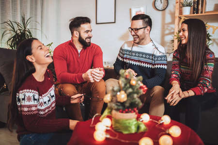 Group of friends sitting in nicely decorated house, having fun while celebrating Christmas or New Yearの写真素材